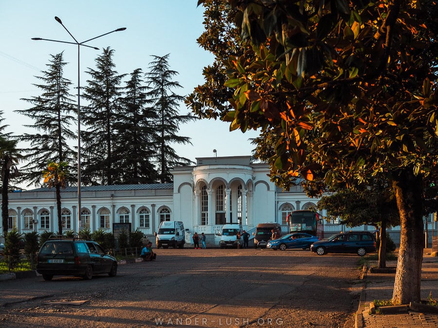 Zugdidi Railway Station, a grand white railway station building framed by golden leaves at dusk.