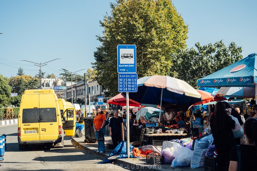 A local bus stop at the market in Zugdidi, Georgia, with yellow vans waiting on the side of the road.