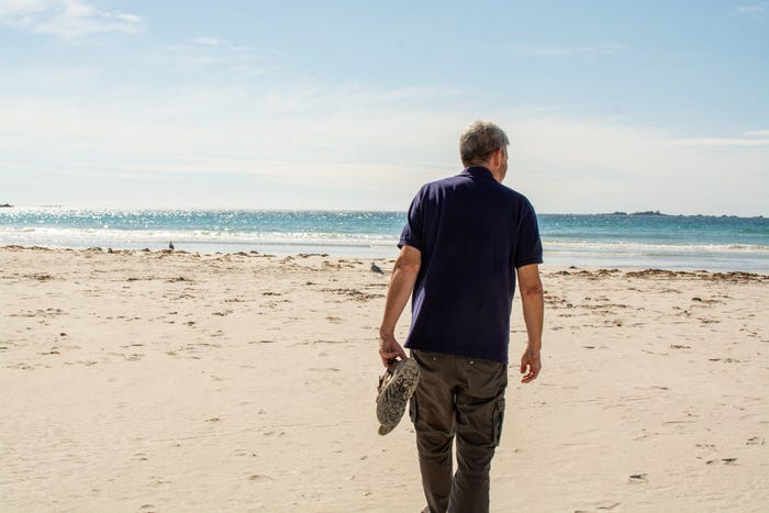 a man walking on the beach, facing away from the camera