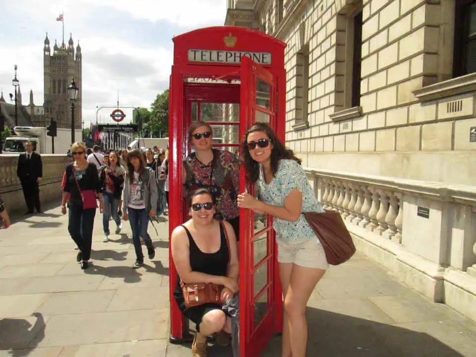 Riana and two friends posing in a red telephone booth in London, England