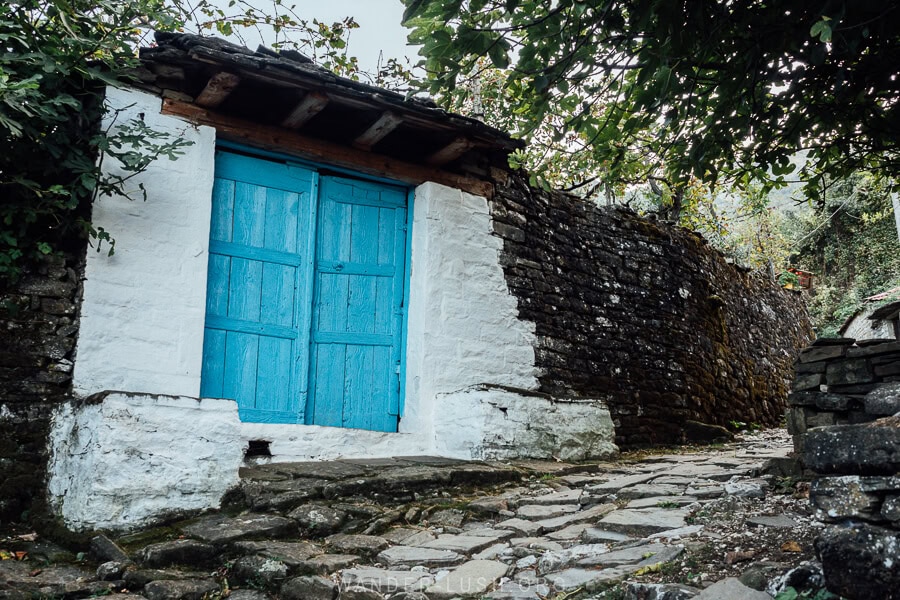 A stone wall with a whitewashed section and a bright blue wooden gate in the village of Leus, Albania.