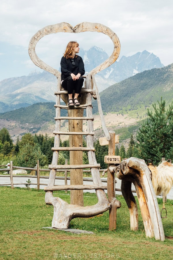 A woman poses for a photo atop a ladder in front of a mountain in Svaneti.