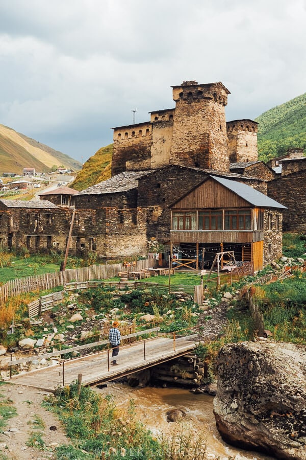 A man crosses a footbridge into a village in Ushguli.