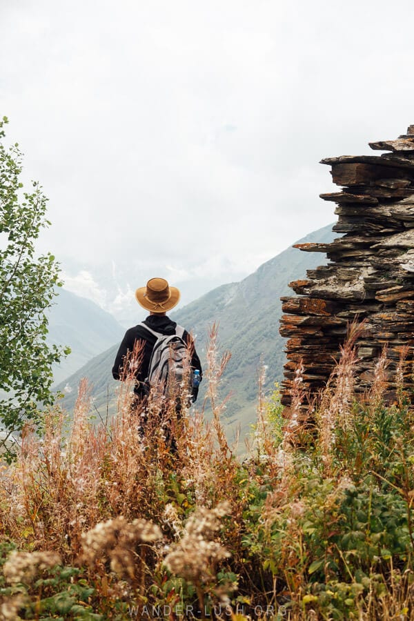 A man in a hiking outfit stands amongst the ruins of an ancient fortress above the village of Ushguli in Georgia.