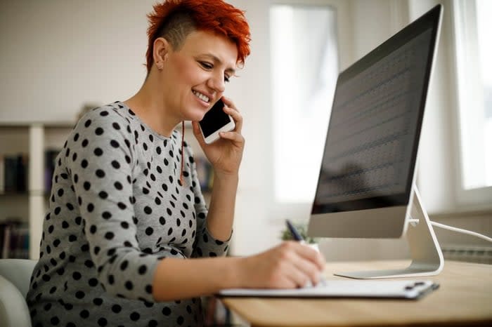 Woman working from home using computer, phone, and laptop.