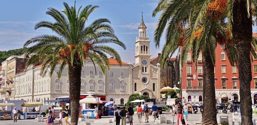 Bustling scene of Split square with people walking around and palm trees against blue skies 