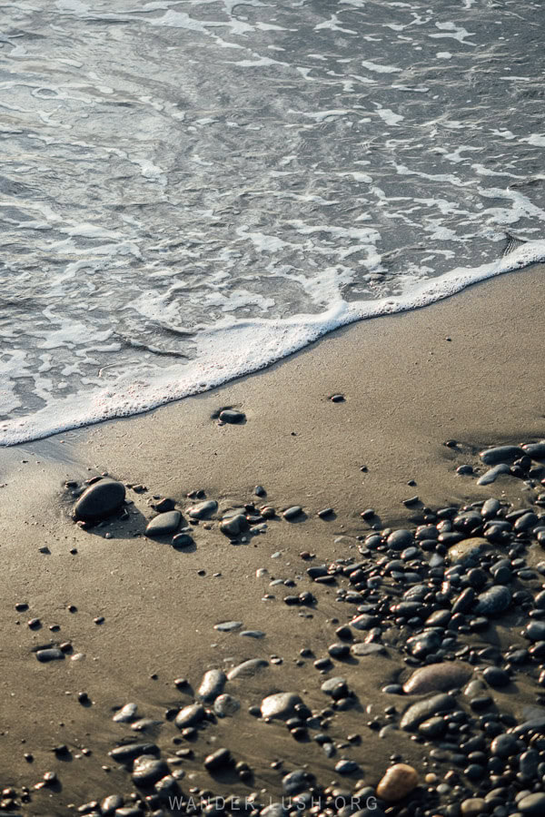 A Black Sea beach in Anaklia, Georgia, with a foamy tide lapping at fine black sands and pebbles on the shore.