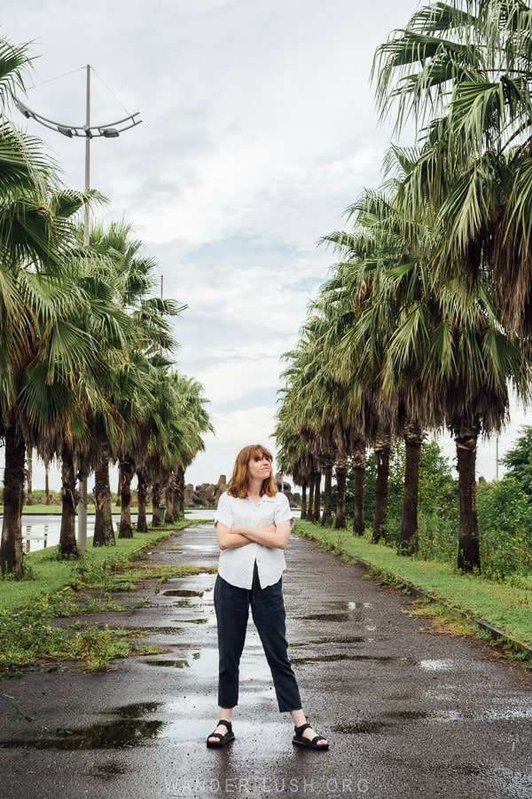 A woman stands on a road in Anaklia surrounded by tall palm trees.