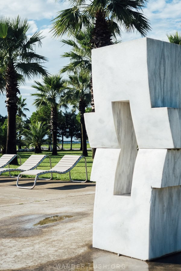 A modern sculpture stands in front of deck chairs and palm trees on the beach boulevard in Anaklia, Georgia.