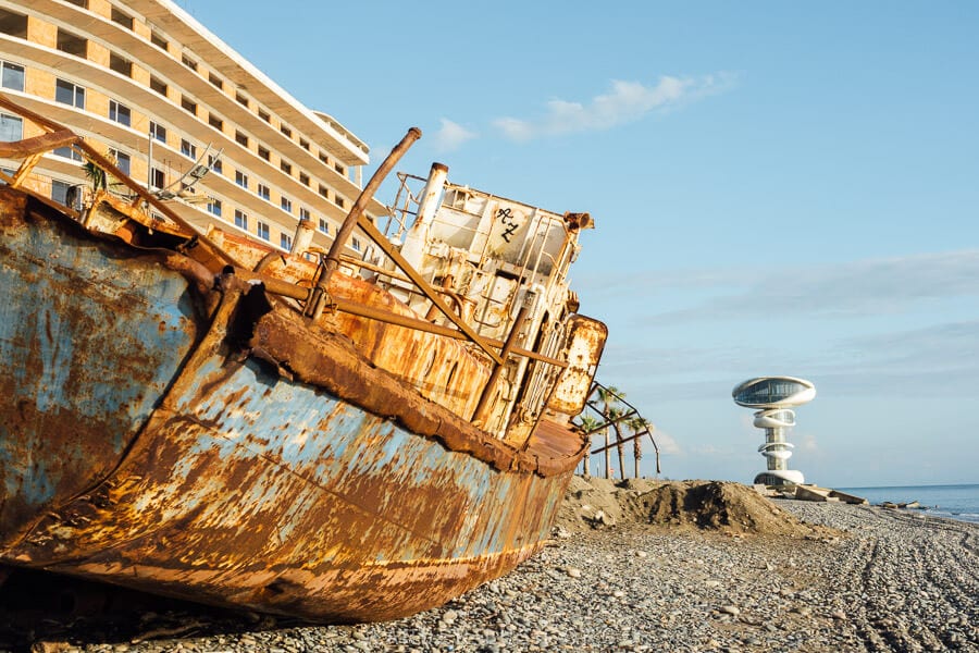 A shipwreck on the Black Sea coast in Anaklia, with a partially constructed resort behind it and the futuristic Anaklia Tower in the distance.