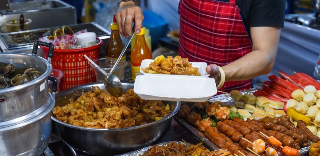 Food vendor serving chicken paws in plastic box with chili in vietnamese night market