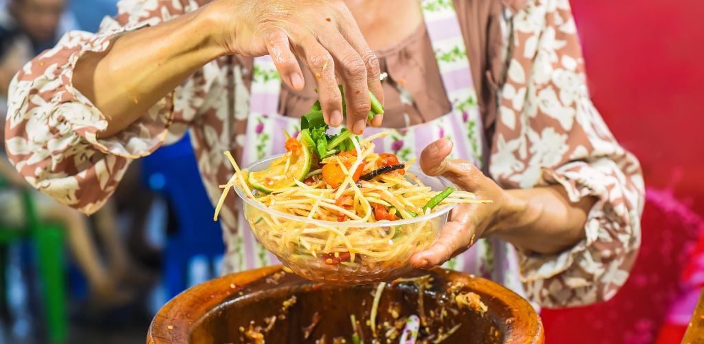 Vietnamese woman serving noodles with traditional, local vegetables and cooking tools