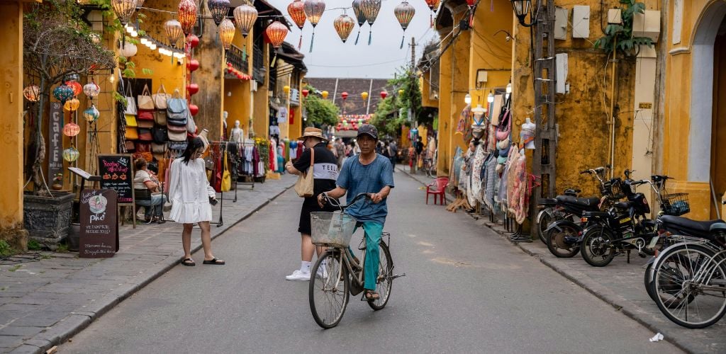 Hoi an, vietnam - the ancient town, man on push bike in middle of street, lanterns seen hanging across buildings 