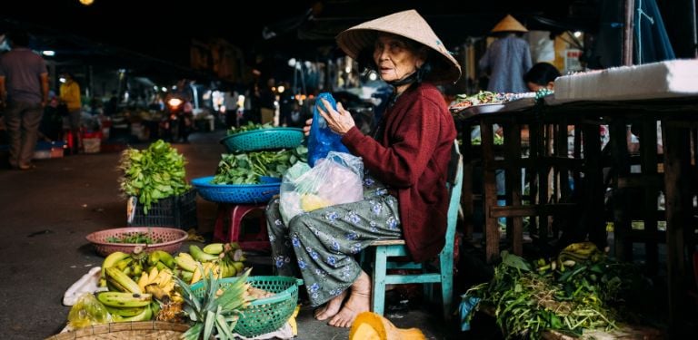 Image of street vendor at night at Vietnamese night market, mixture of local fruit and vegetables surround the vendor 