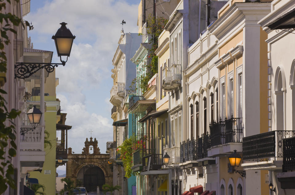 Street view of colorful buildings in San Juan, Puerto Rico, with ornate balconies and a gate in the background.