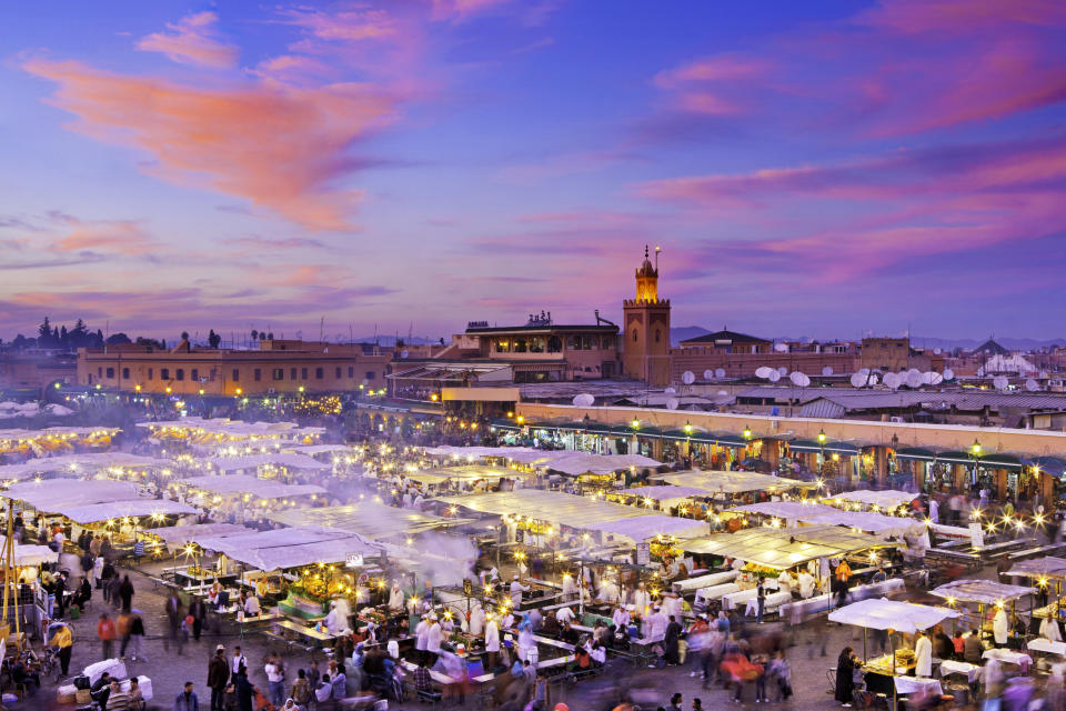 A bustling market square in Marrakech at sunset, with vibrant stalls and people roaming.