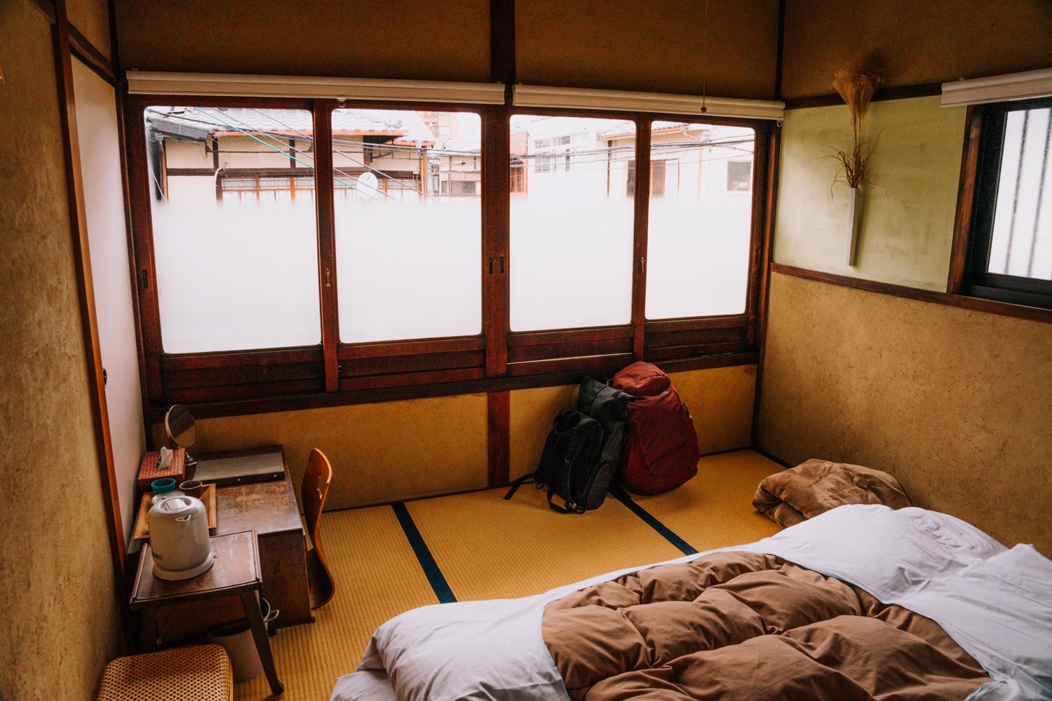 Inside a traditional Kyoto machiya townhouse hotel with a futon bed, small desk, and digital nomad backpacks.