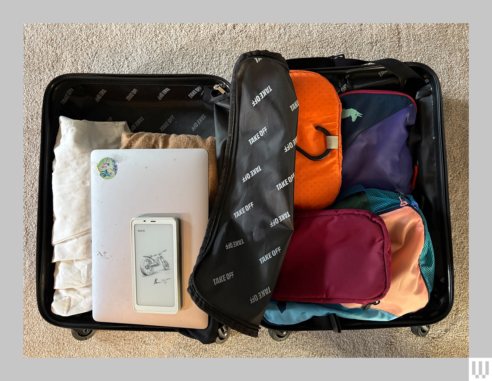 Overhead view of a small rolling suitcase fully opened to show clothing laptop packing cubes and mobile phone inside