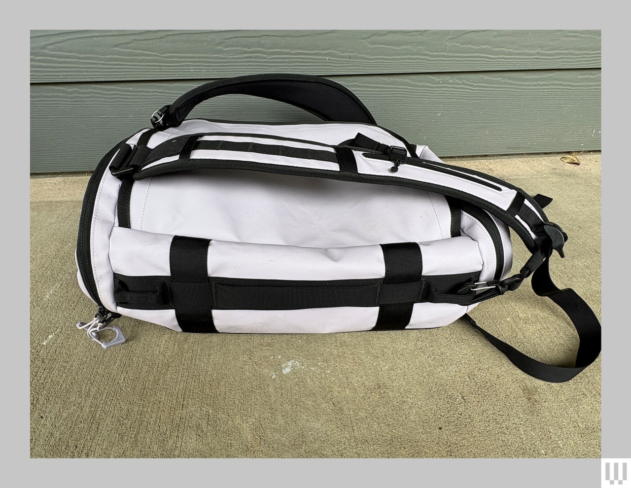 Wandrd Carryall Duffel, a small black and white bag with thick straps. sitting on concrete