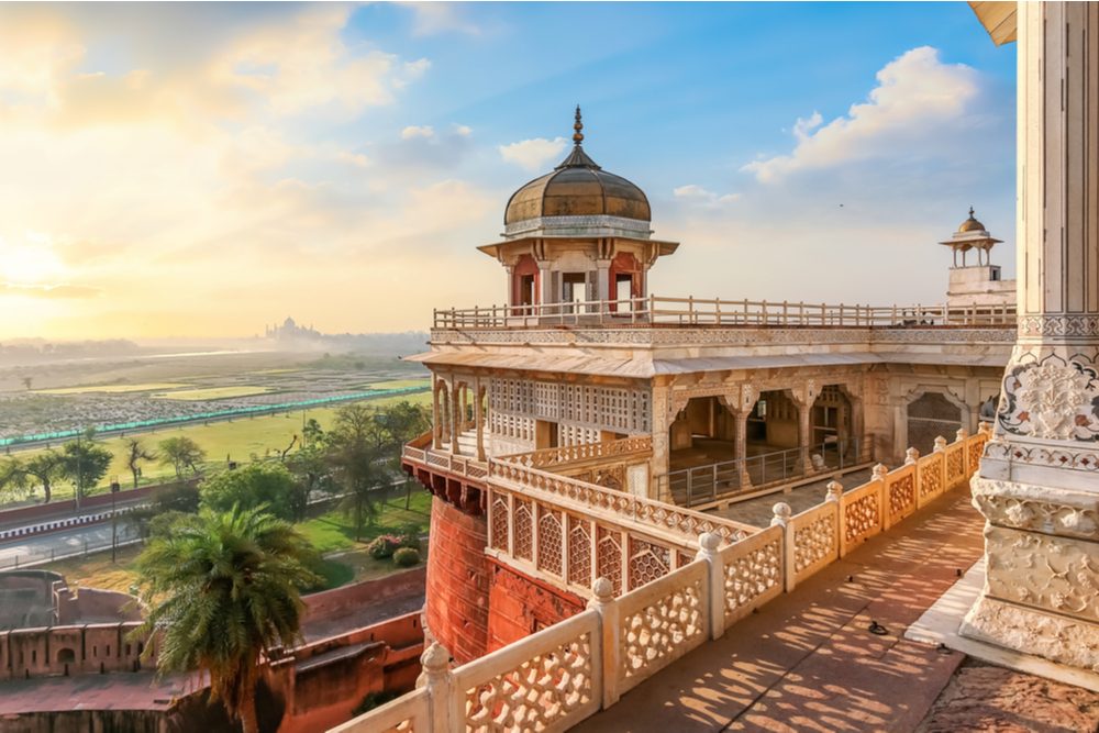 Agra Fort - Medieval Indian fort made of red sandstone and marble with view of dome at sunrise. View of Taj Mahal at a distance as seen from Agra Fort.