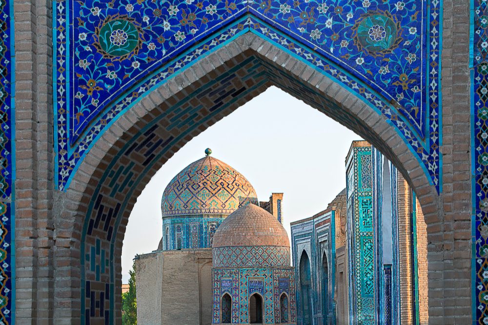 View over the mausoleums and domes of the historical cemetery of Shahi Zinda through an arched gate, Samarkand, Uzbekistan.