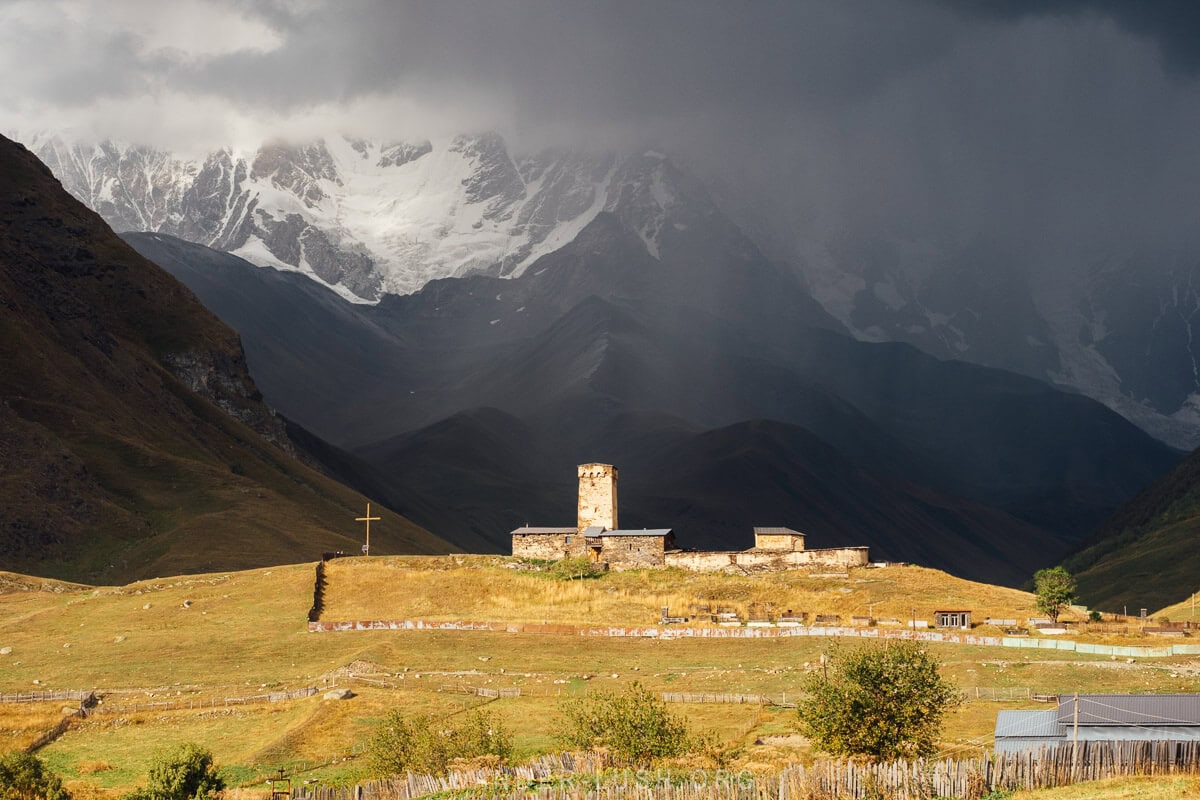 Lamaria Church in Ushguli on a moody evening, with Shkhara mountain visible through the clouds.