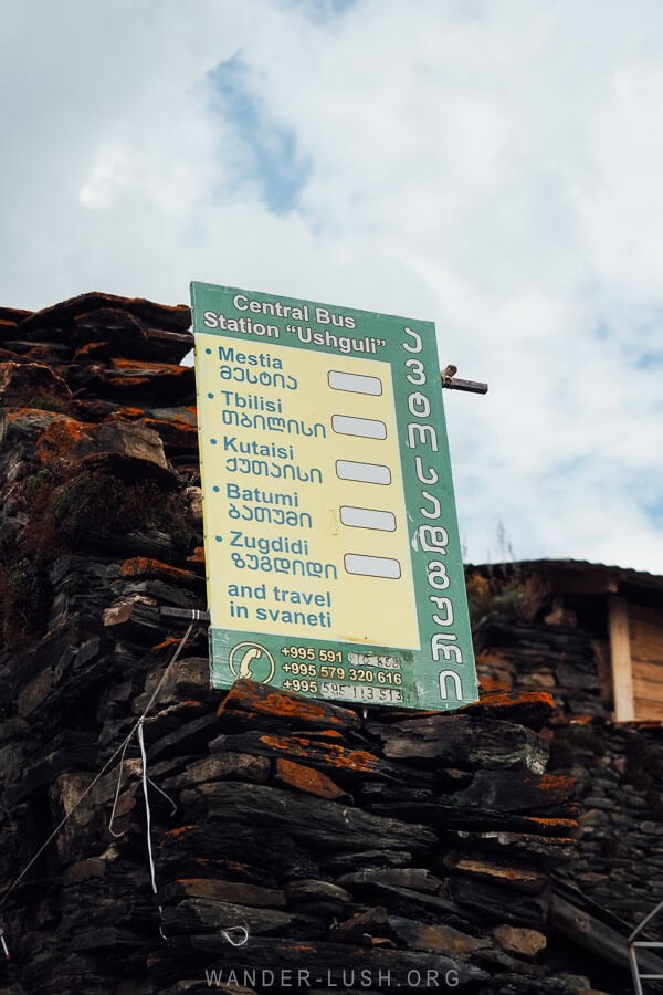 A small bus station in Ushguli, Georgia with a sign reading the different destinations of Tbilisi, Batumi and Zugdidi.