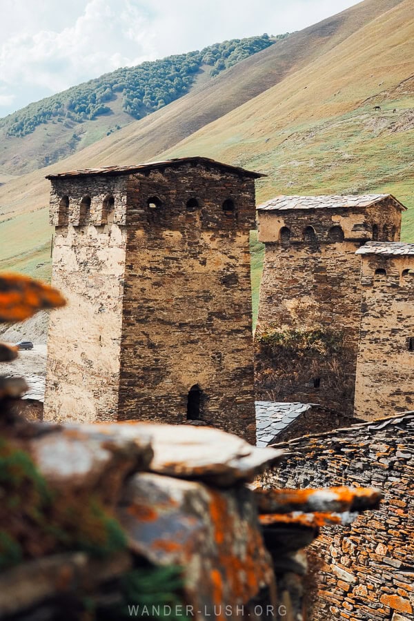 The tops of three stone towers in Ushguli seen against a backdrop of mountains in autumn.