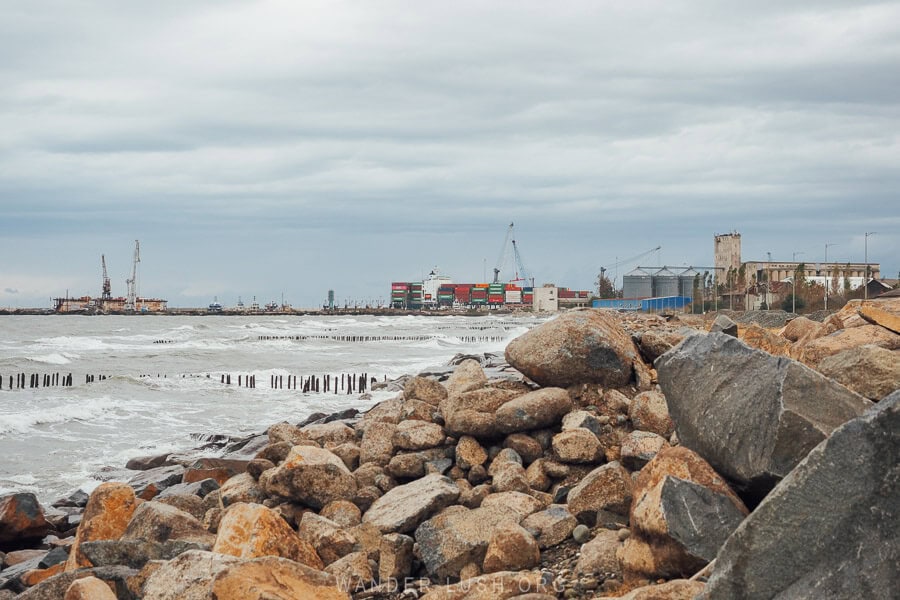 A rocky shore with seaport cranes and containers in the distance on the coast at Poti.