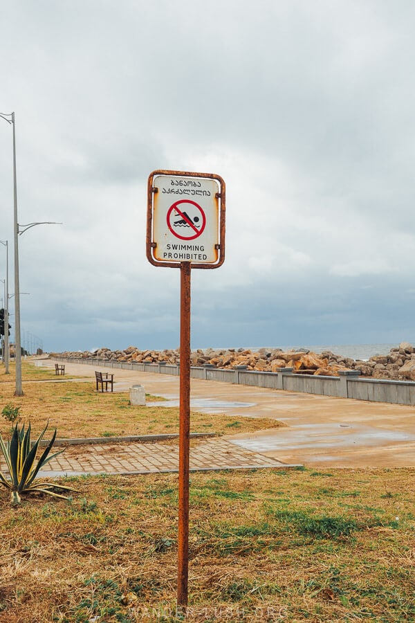 A swimming prohibited sign stands on the boulevard in Poti against a grey sky.