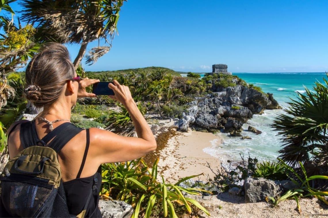 Girl taking a picture of the Mayan archealogical site next to the beach in Tulum