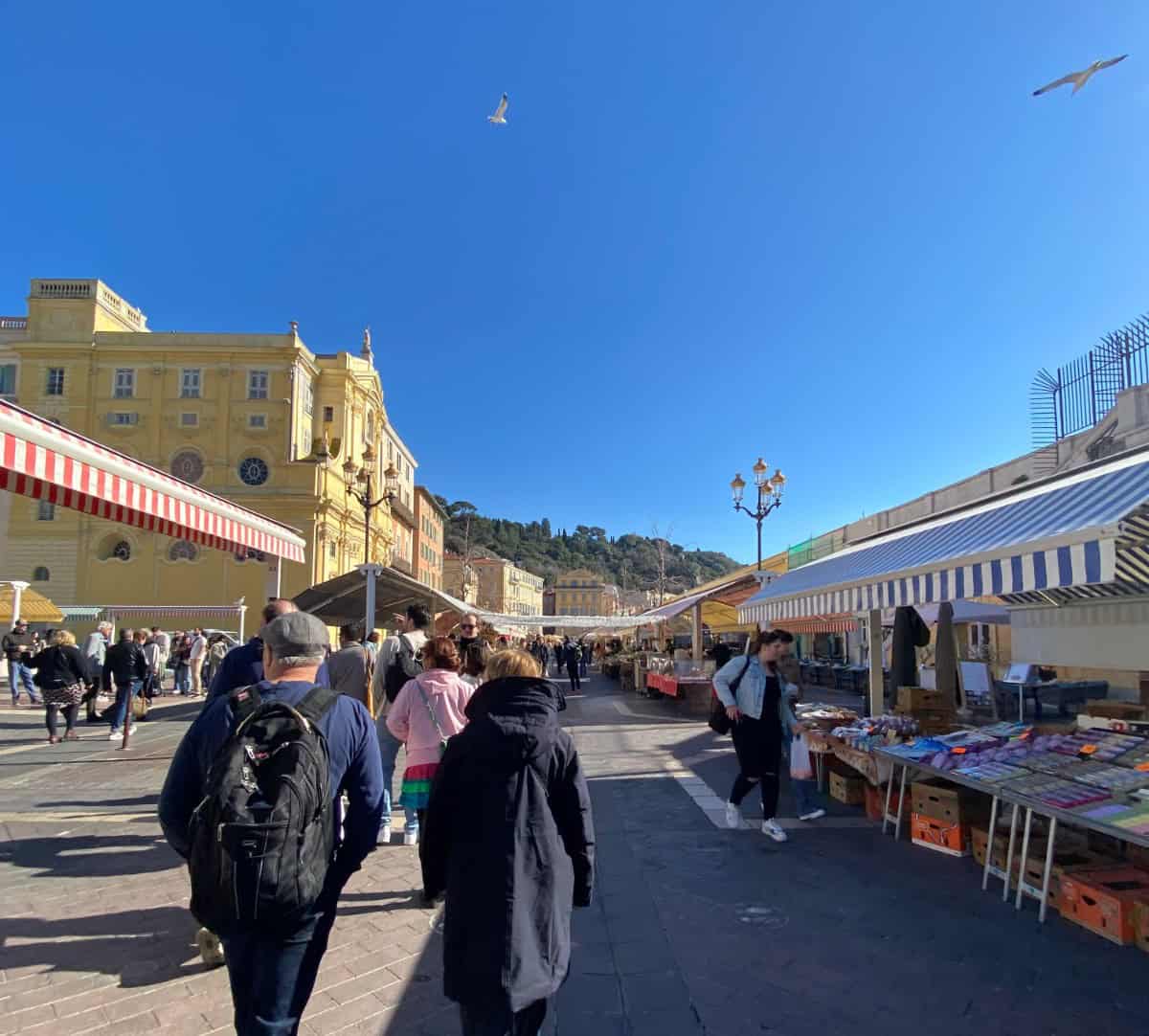 Walking through the Cours Saleya market in Nice, France with fellow pedestrians and stalls along the side of the street