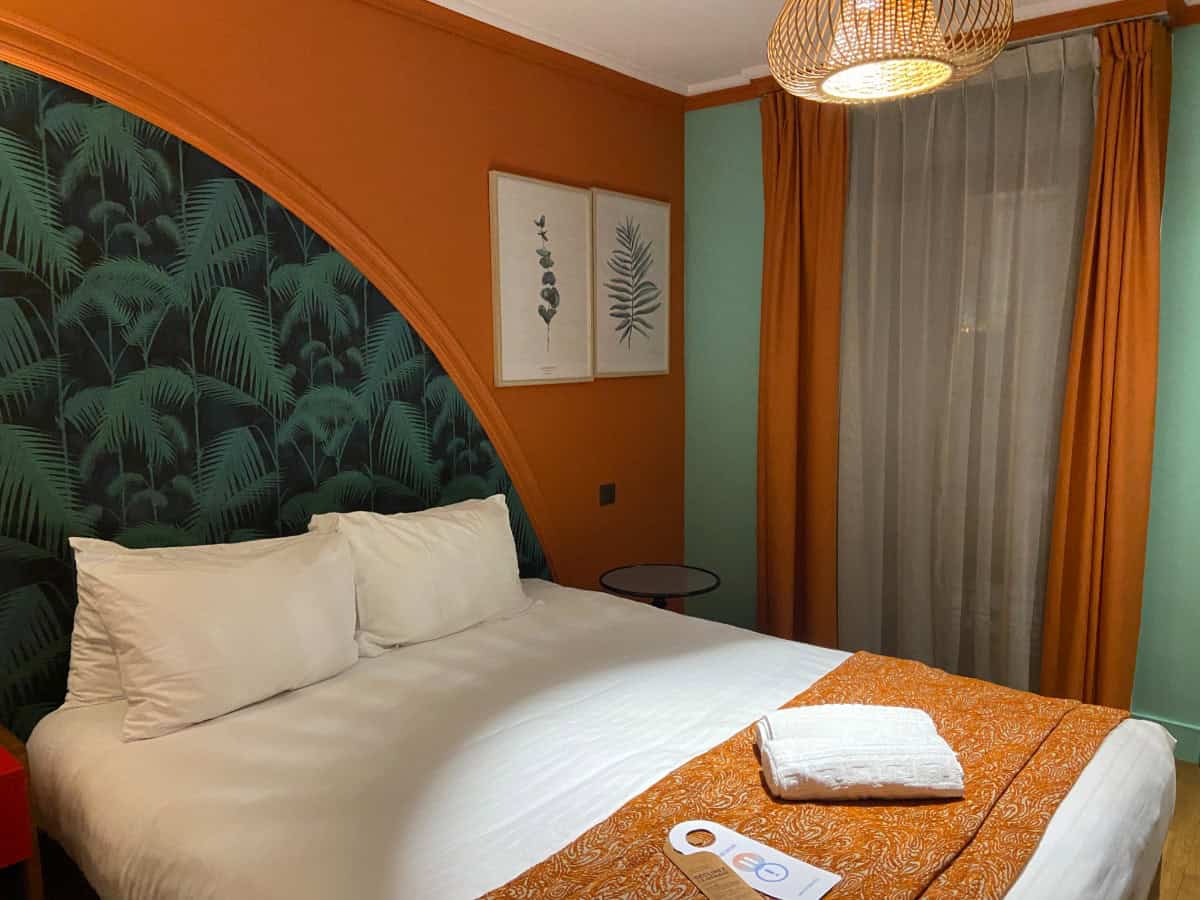 Our hotel room in Nice at the Villa Bougainville by Happy Culture showing a white bed with orange accents, orange walls and a green headboard