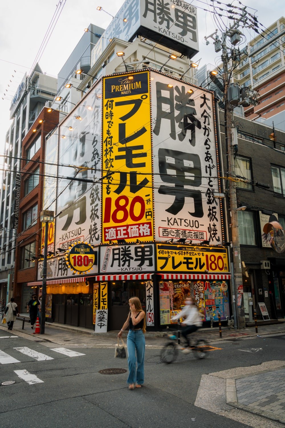 A tourist crosses the street in front of Japanese shop with yellow sign in Osaka, Japan.