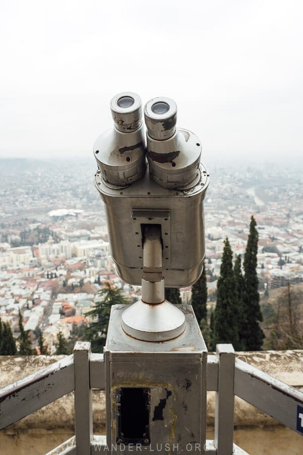 A pair of silver binoculars mounted to a viewpoint above Tbilisi.