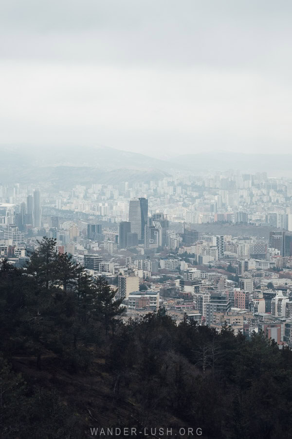 A view of Tbilisi in winter, with a dark forest and misty clouds over the city.