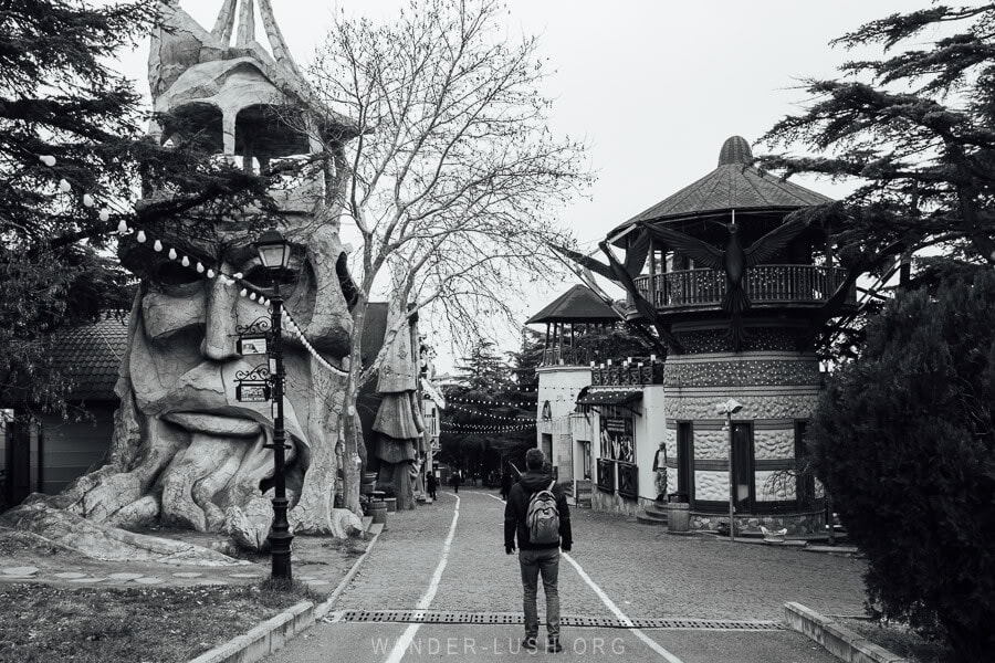 A man standing in front of a building shaped with an old man's face and beard inside Mtatsminda Park, Tbilisi.