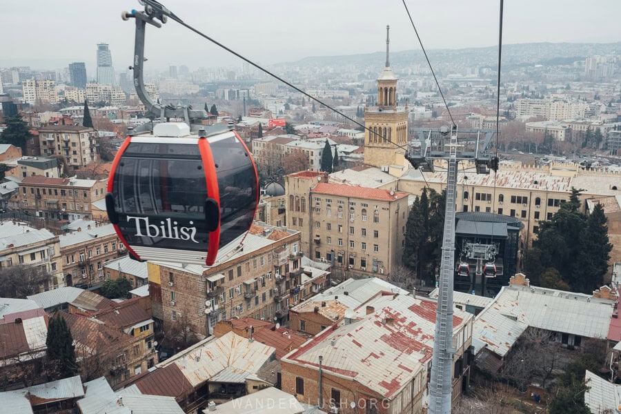 A modern black and red gondola flies above the city of Tbilisi from a renovated station off Rustaveli Avenue towards Mtatsminda Park.