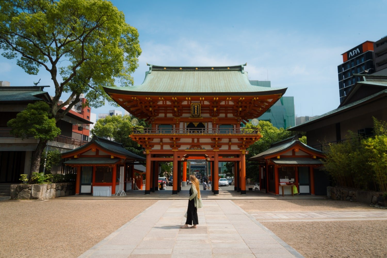 Tourist and travel blogger (Bucketlist Bri) at Ikuta Jinja, Shinto Shrine in Kobe, Japan with red temple and spacious plaza.