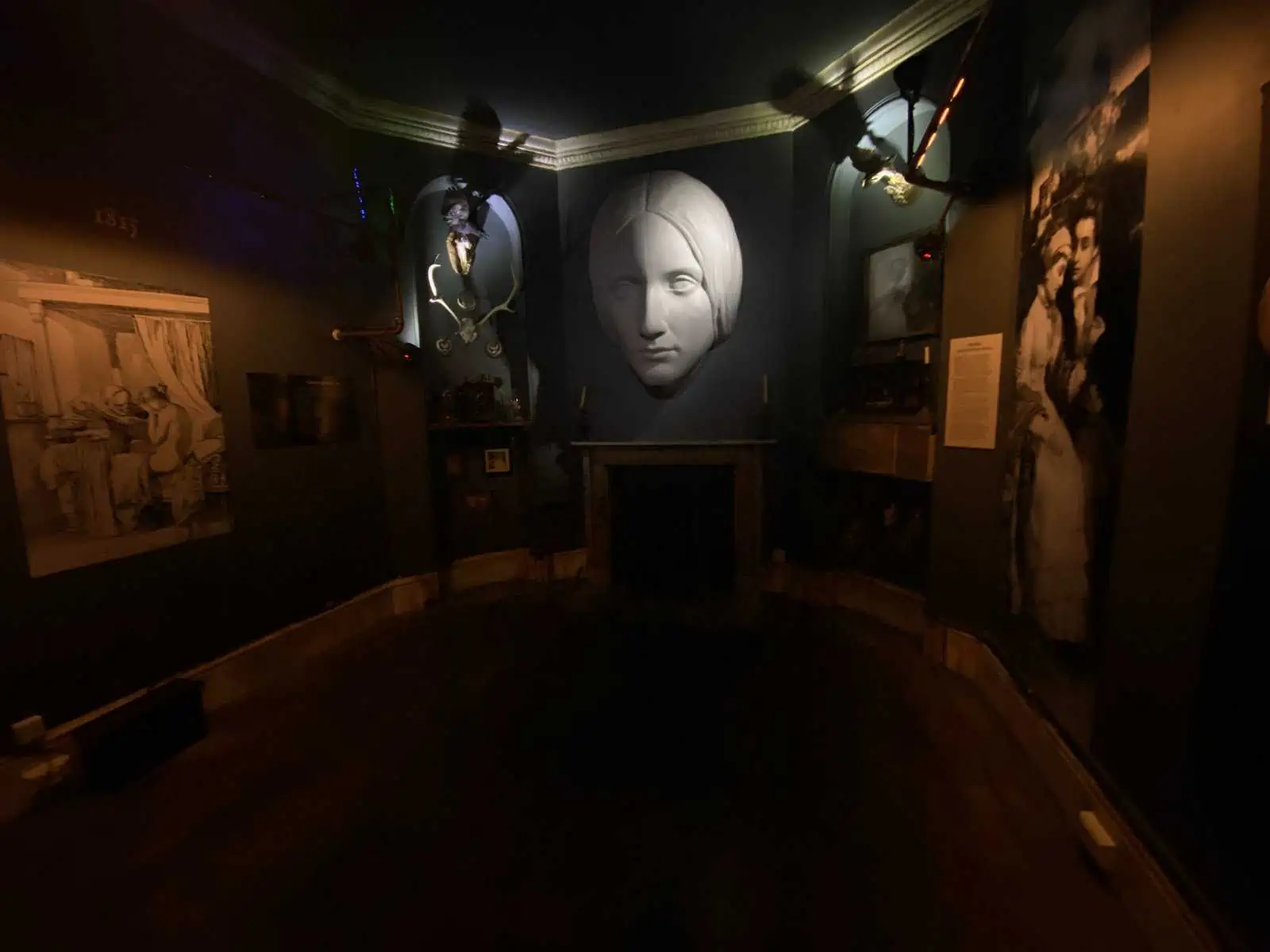 Inside one of the rooms at Mary Shelley's House of Frankenstein in Bath, England. The room is dark and there's a large white moulding of a face on the wall. 