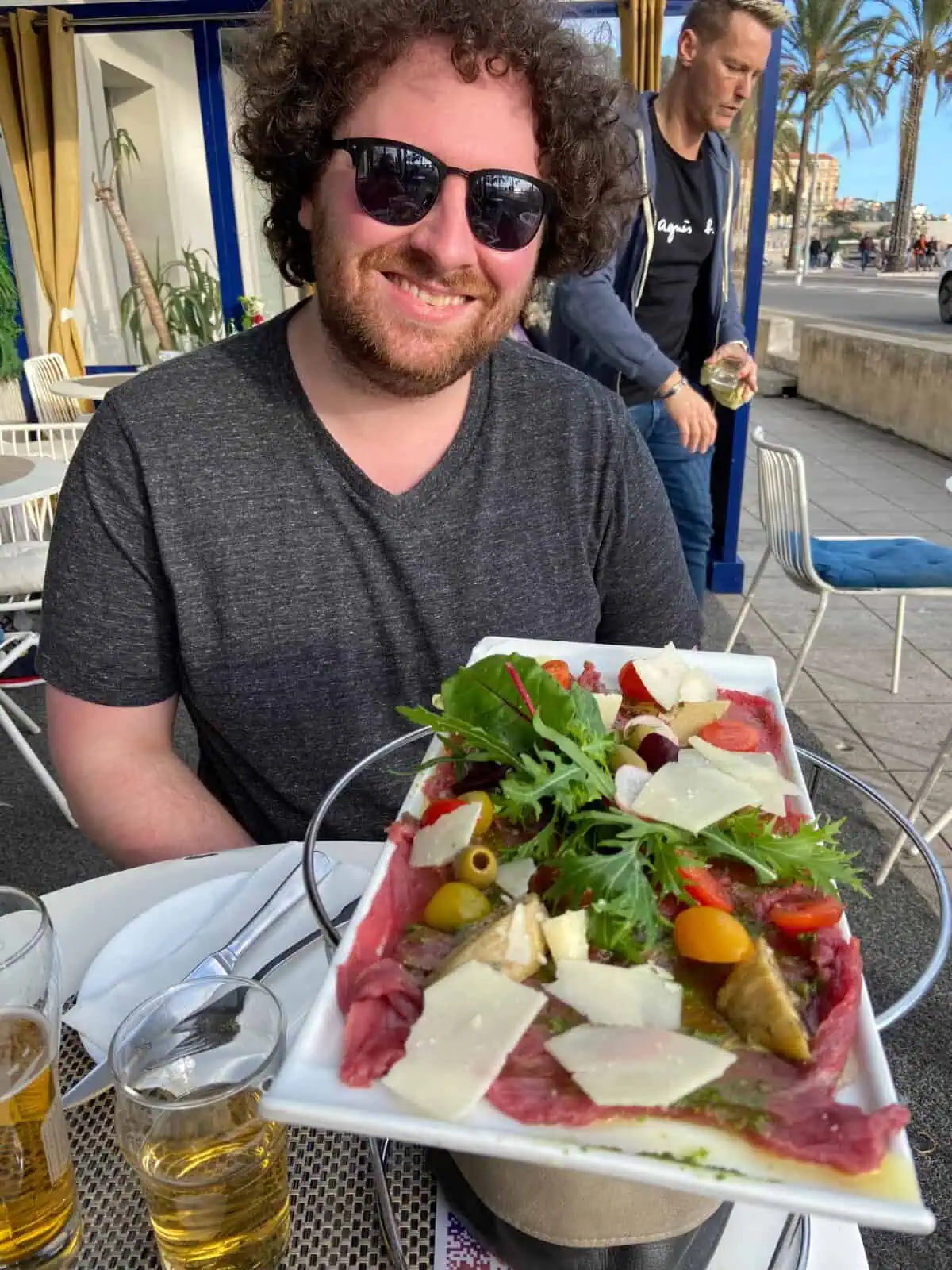 Colin smiling in front of a platter of beef carpaccio and cheese with greens on top