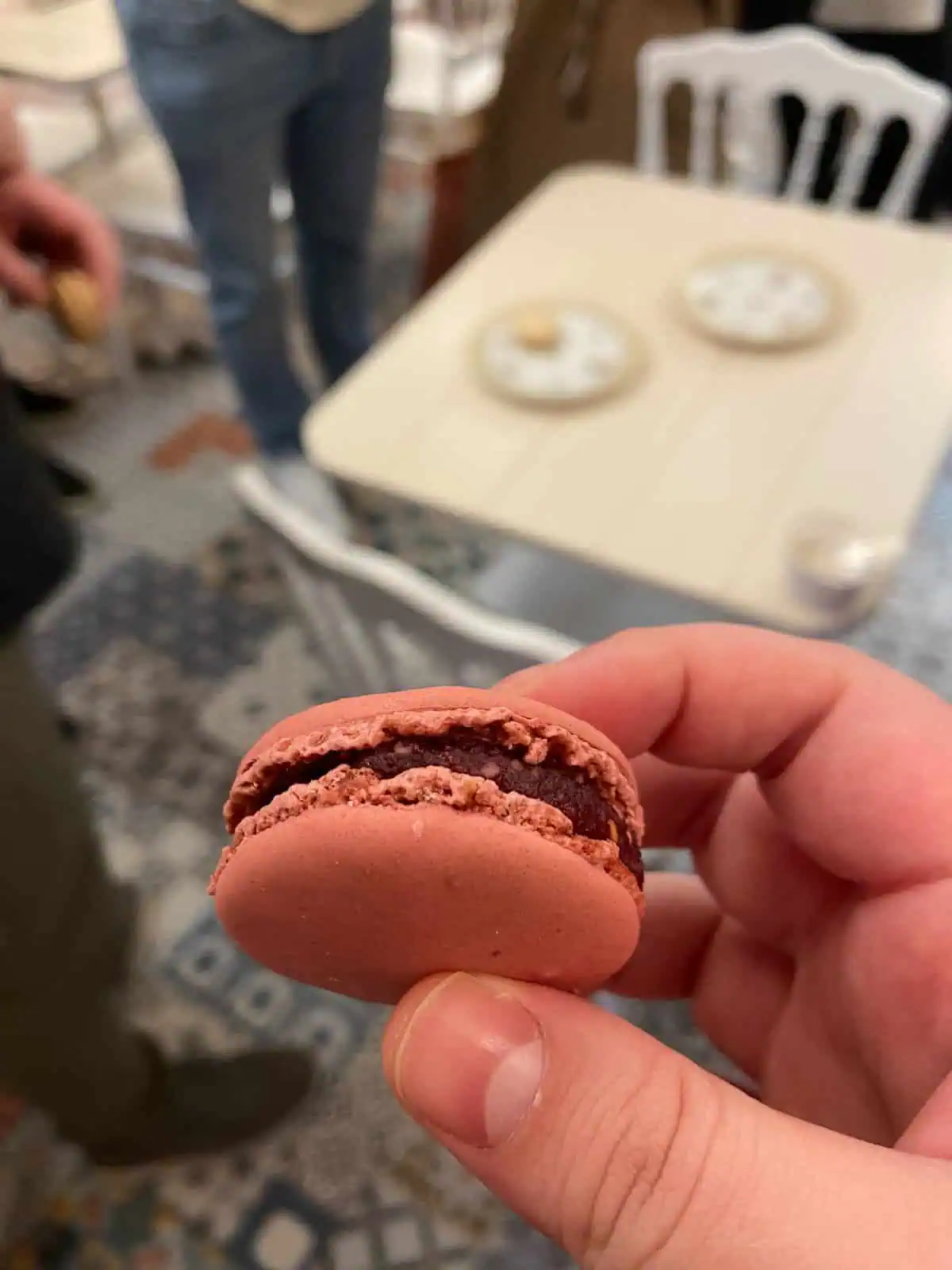 Riana holding a raspberry macaron inside a macaron shop in France