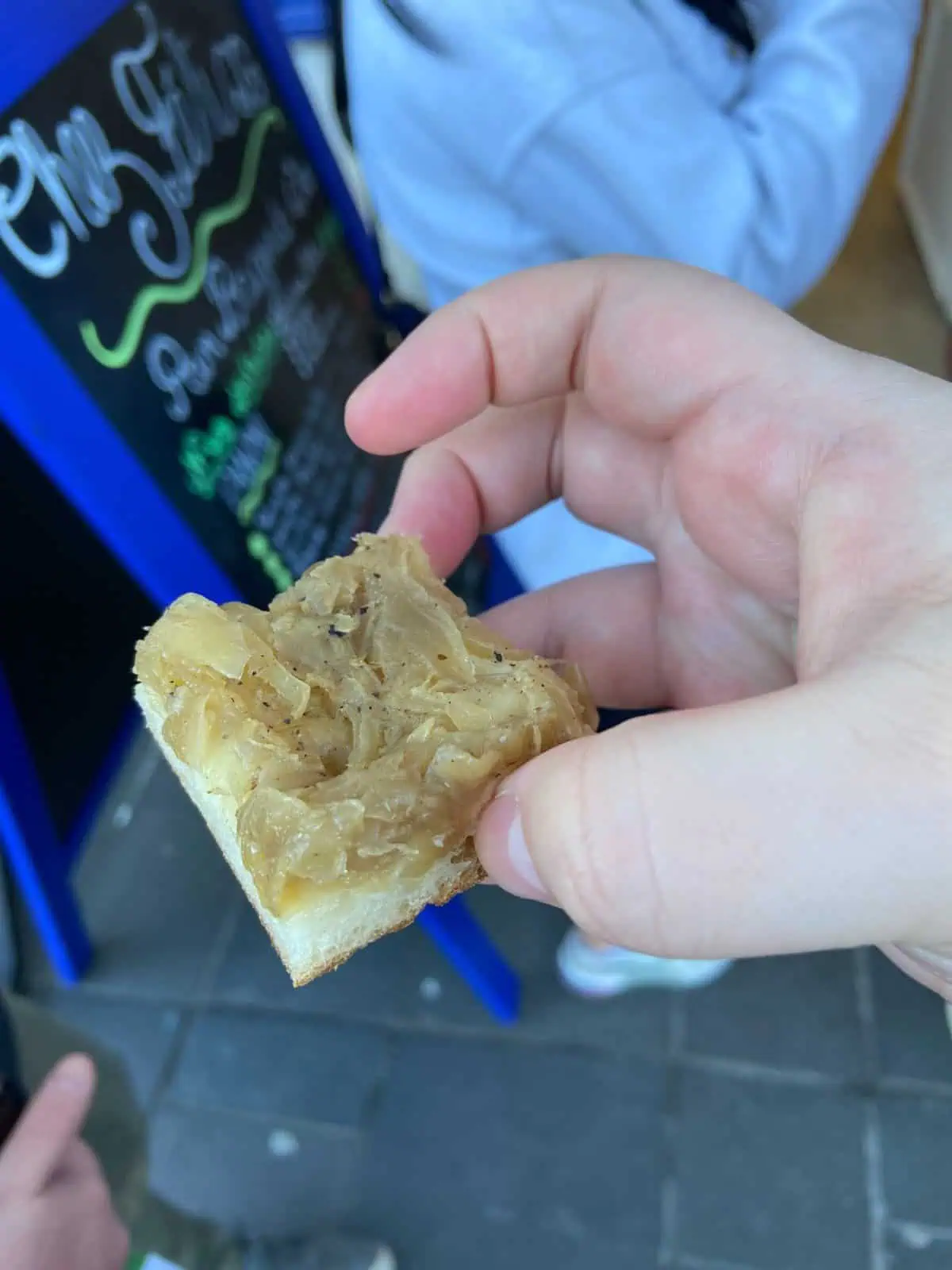 Holding a piece of Pissaladière, a must try food from Nice where a pastry is topped with onions