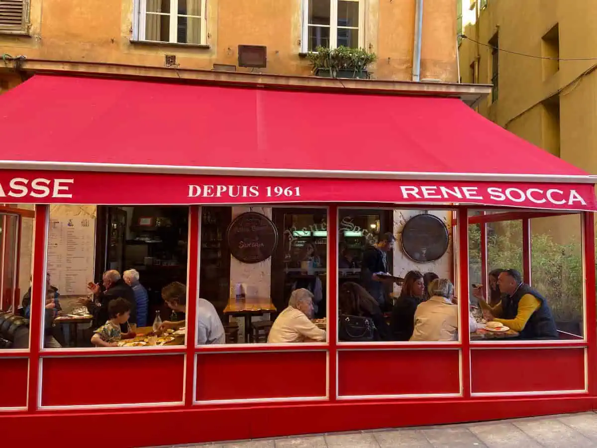 Outdoor dining area covered in a red awning of Rene Socca, serving up socca and fried street food in Nice