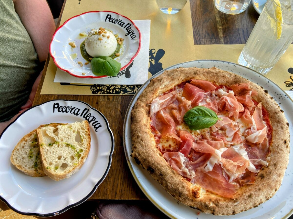 A table full of Italian food eaten in Menton France: mozarella, bread and a pizza with ham