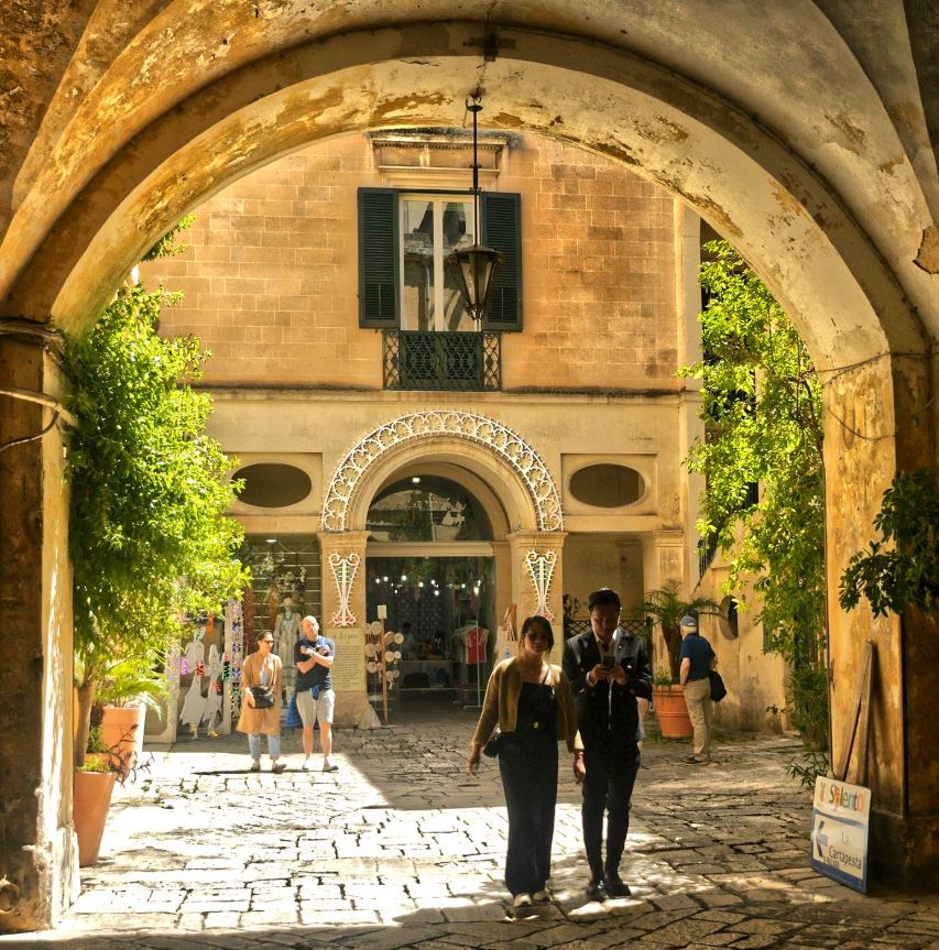 People walk under an archway as others stand in the background.