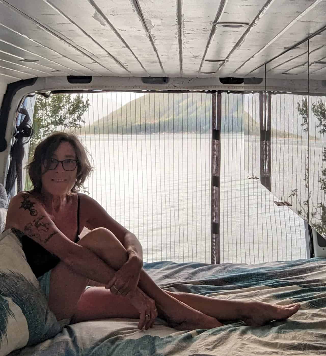 Lyn on the bed in her campervan parked at Arrow Lakes Provincial Park