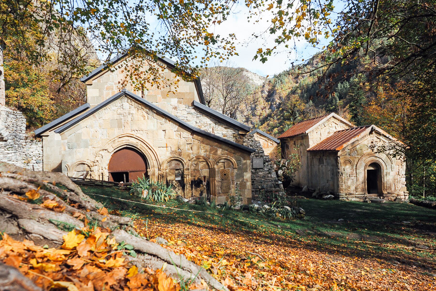 Rkoni Monastery, an ancient stone church flanked by tall trees and autumn leaves.