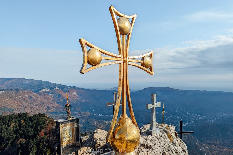 A mountain summit with a large gold cross planted in the rock. Tskhrajvari viewpoint near Tkibuli in Georgia.