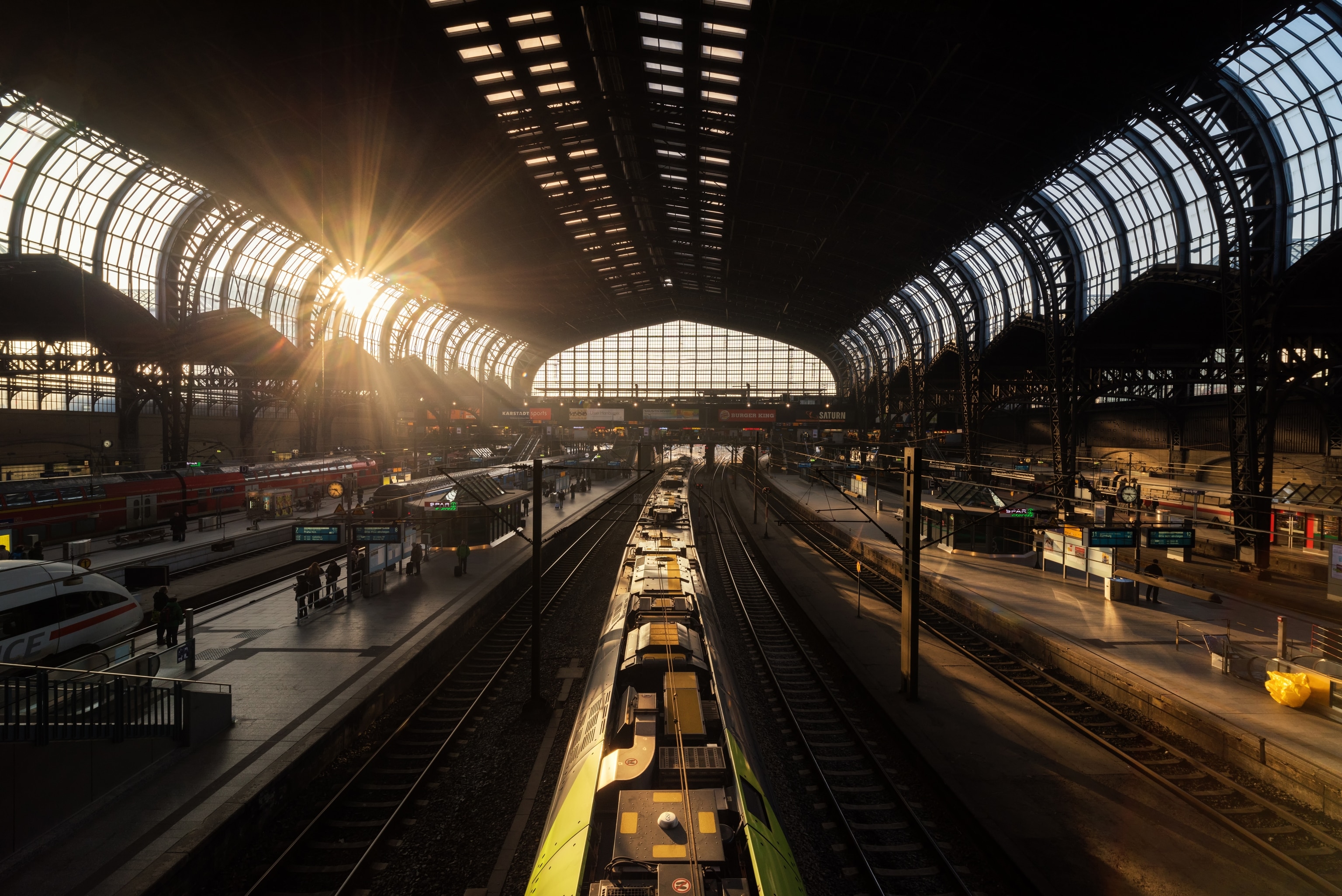 An interior view into a busy, arched train station at sunset.